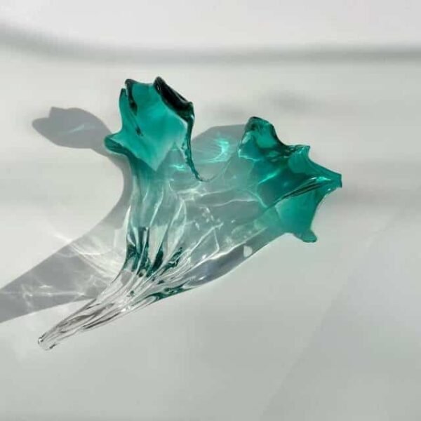 Elegant Aqua Green Glass Leaf Centerpiece - Handcrafted Glass Decor A stunning glass centerpiece resembling a leaf, featuring a translucent aqua green design that flows elegantly into clear glass, capturing light and shadows beautifully. The piece showcases sophisticated glass craftsmanship with organic curves and handcrafted details, perfect as a decorative element. Ideal for showcasing unique glass decor in any setting.