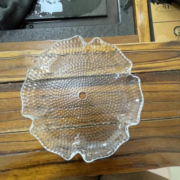 A detailed view of a pressed glass dish featuring a textured, floral design with small bubbles and a central hole. The clear glass showcases a wavy edge, enhancing its decorative appeal. This piece exemplifies precision and uniformity characteristic of pressed glass, ideal for elegant table displays.
