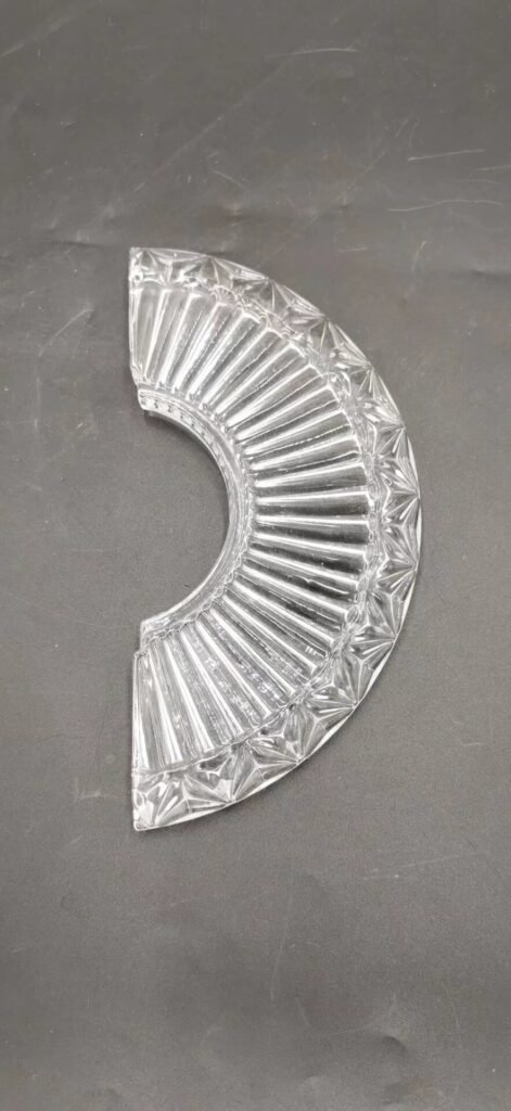 A beautifully crafted glass lamp base features a fan-shaped design, showcasing ridged textures and sharp-edged patterns that catch light beautifully. The glass is clear with an intricate design, highlighting the craftsmanship and unique characteristics typical of pressed glass manufacturing. Ideal for pairing with lamp fixtures, this piece adds elegance and functionality to interior decor.